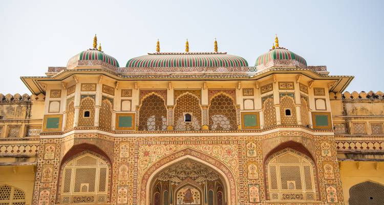Voorkant van het Amber Fort met gestreepte koepels en opzichtige fresco's tegen een bleek lucht.
