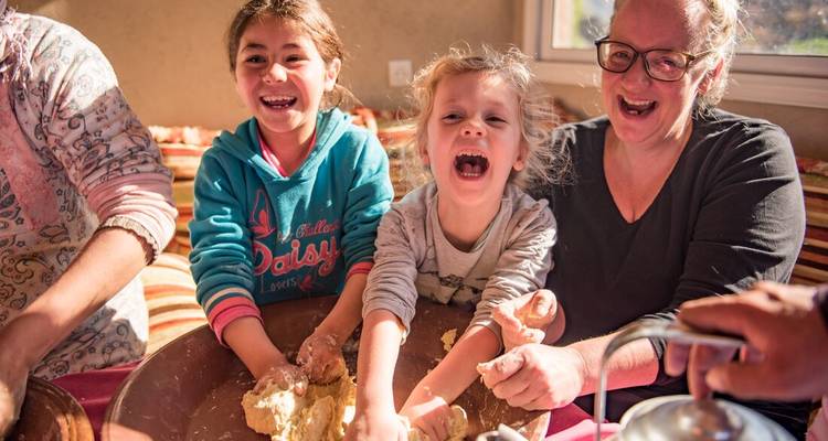 Niños y padres riendo mientras amasan la masa juntos en una cocina marroquí iluminada por el sol.