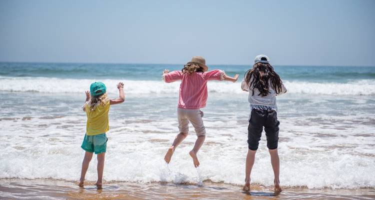 Tres niños saltando alegremente sobre las olas que llegan en una playa soleada.