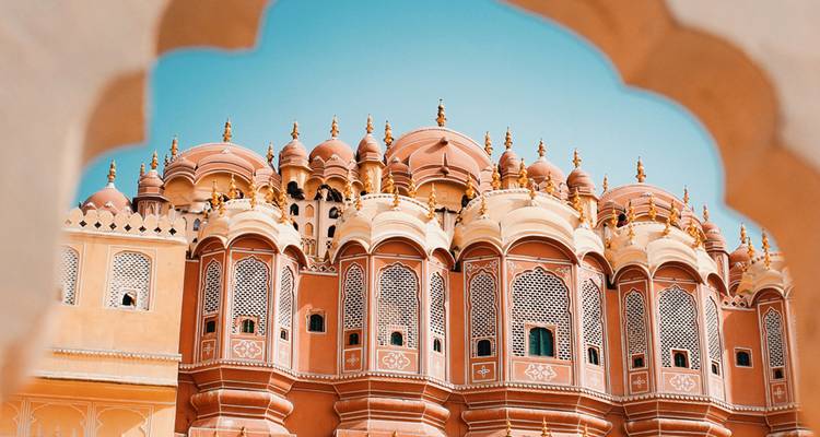 Façade rose vif et ocre du Hawa Mahal encadrée par une arche décorée sur un ciel turquoise.