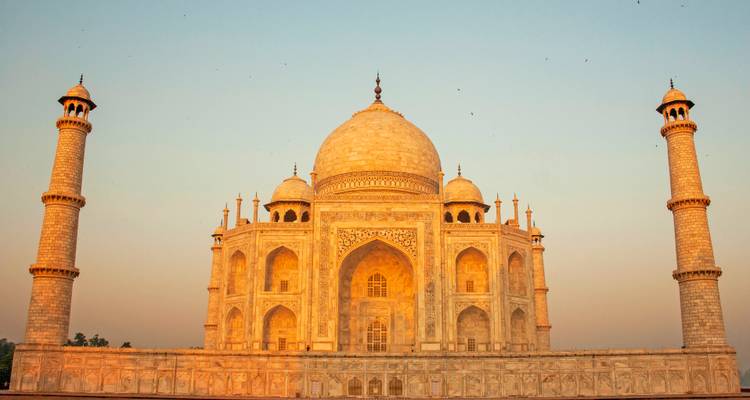 Le Taj Mahal illuminé par la lumière chaude de l'aube avec un ciel aux tons pastel et des minarets symétriques.