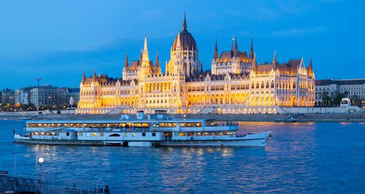 Parlement hongrois illuminé à l'heure bleue avec un bateau de croisière fluviale glissant sur le Danube.