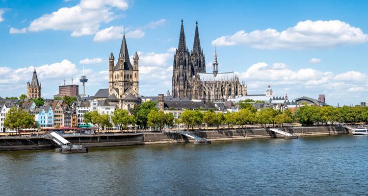 Vue panoramique du large Rhin avec la Cathédrale de Cologne et la Grande Église Saint-Martin sous un ciel d'été bleu.