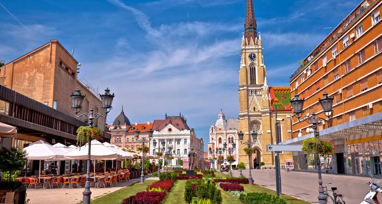 Plaza peatonal vibrante en Novi Sad con la Iglesia del Nombre de María y cafés al aire libre.