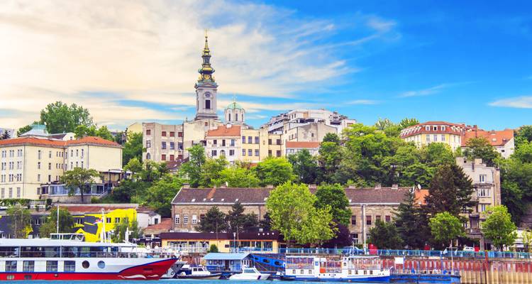 Skyline de la margen del río de Belgrado con campanario de iglesia histórica y casas coloridas con cielo azul de fondo.