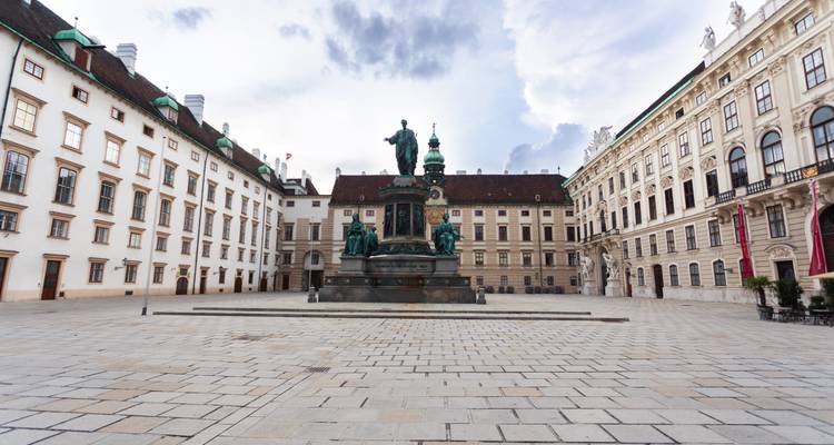 Patio vacío del Palacio Hofburg de Viena con una estatua de bronce monumental bajo un cielo nublado y dramático.