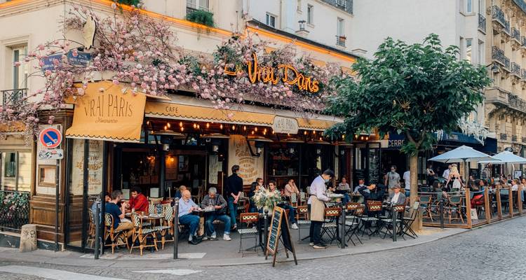 Encantador bistró de barrio en París con árboles rosas en flor y mesas al aire libre donde los lugareños se relajan.