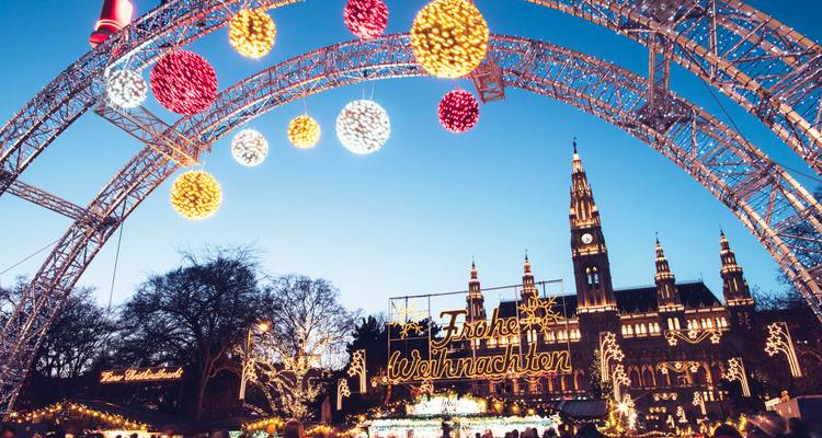 Mercado navideño festivo de Viena en la Rathausplatz con luces brillantes, bolas de colores y el ayuntamiento iluminado de fondo.