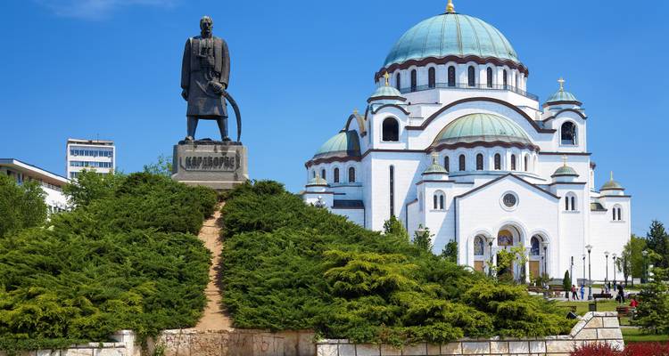 Cúpulas blancas del Templo de San Sava con la estatua de Karadjordje y exuberante vegetación al frente