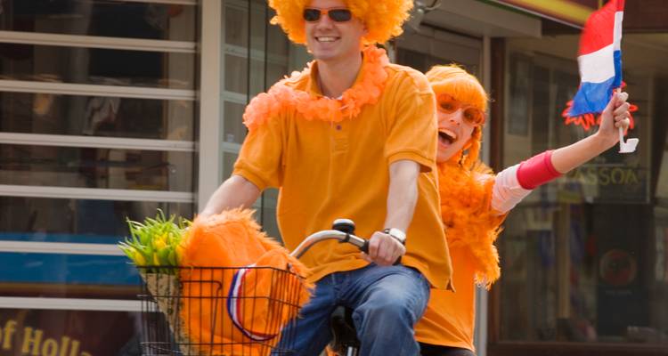 Fröhliche Radfahrer in orangefarbenen Kostümen winken niederländische Flaggen während der Feierlichkeiten zum Königstag.