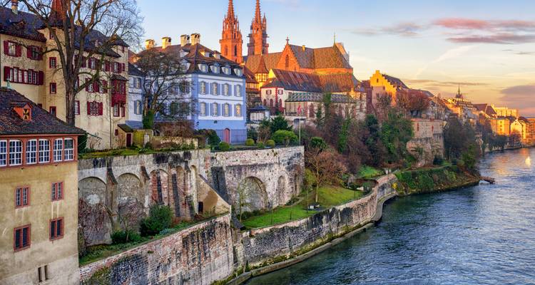 Goldenes Abendlicht auf den Häusern am Rhein in Basel und der Kathedrale über den Steinmauern.