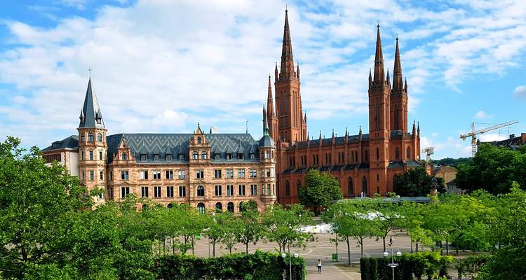 Église néo-gothique en brique rouge et palais adjacent s'élevant au-dessus d'un parc urbain verdoyant à Wiesbaden