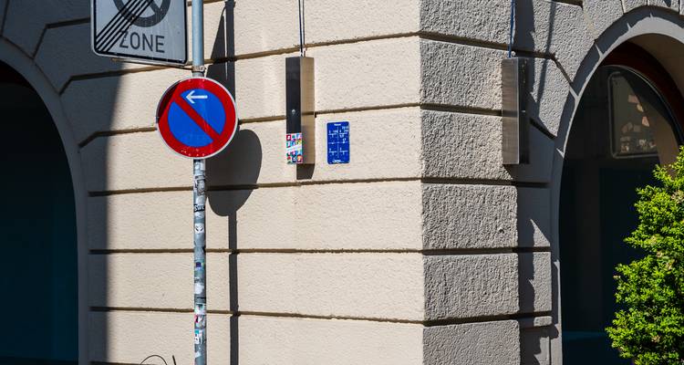 Coin de rue avec un mur beige, un panneau de signalisation routière avec une flèche bleue et une ombre.