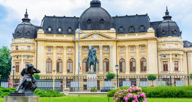 Bibliothèque universitaire centrale de Bucarest de style néoclassique et statue équestre précédées d'une pelouse soignée.