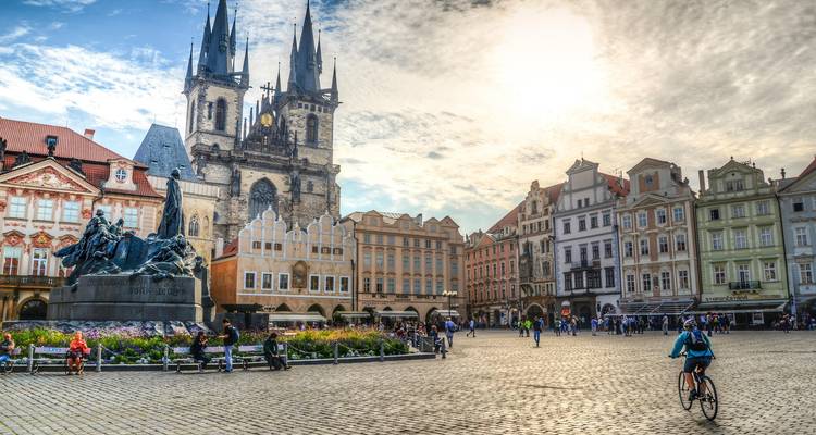 Scène diurne ensoleillée de la Place de la Vieille Ville de Prague avec des cyclistes, des touristes et l'Église Notre-Dame de Týn