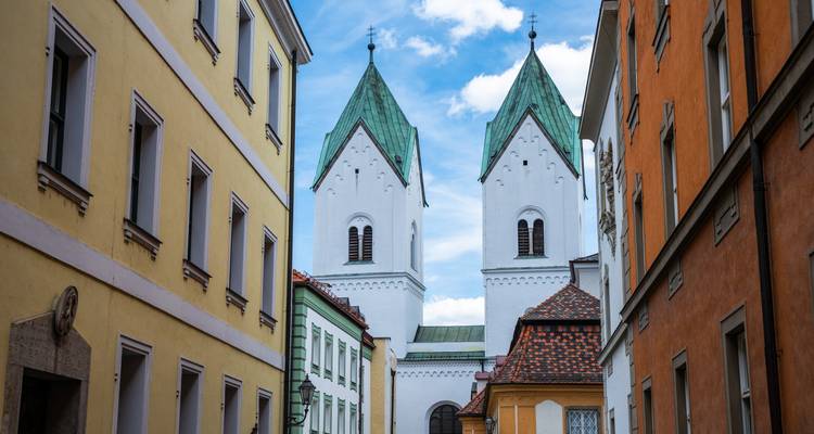 Callejón estrecho europeo rodeado de casas coloridas que lleva a una iglesia blanca con dos torres