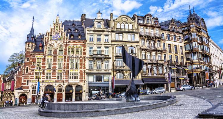 Elegante Reihe eckelhafter historischer Fassaden mit Blick auf eine kleine moderne Brunnen-Skulptur unter einem leuchtenden Himmel.