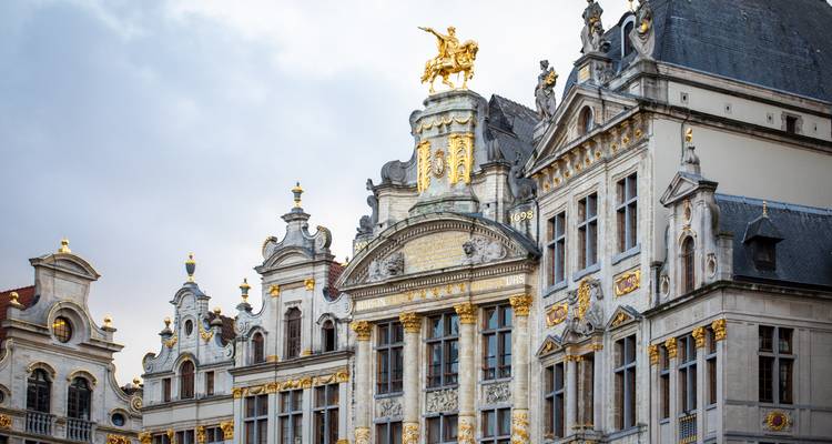 Nahaufnahme von prunkvollen Zunfthäusern mit vergoldeten Statuen und barocken Details vor einem stimmungsvollen Himmel.