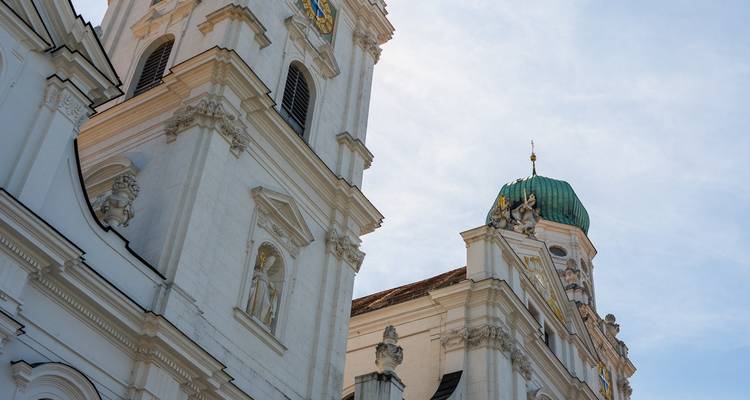 Tour d'église baroque blanche avec dôme en cuivre vert sur un ciel clair.