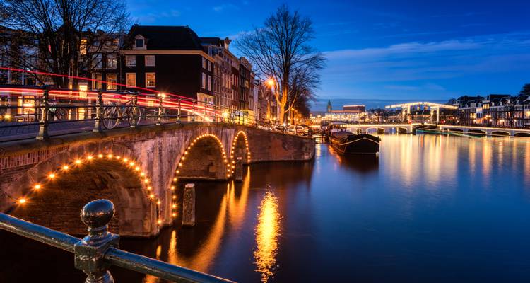Escena nocturna de puentes iluminados y aguas azules tranquilas a lo largo del famoso anillo de canales de Amsterdam.