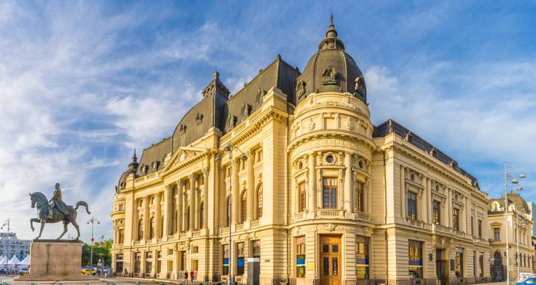 Vue diurne de la Bibliothèque centrale de l'Université de Bucarest avec statue équestre sous un ciel bleu.