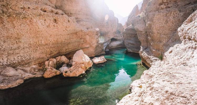 Piscine turquoise parsemée de taches de soleil nichée dans les gorges rocheuses de Wadi Shab.