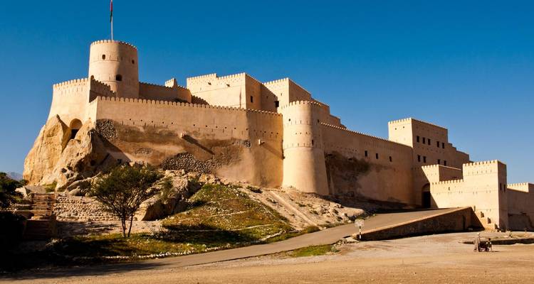 Imposante forteresse de couleur sable se dressant contre un ciel omanais d'un bleu cristallin.