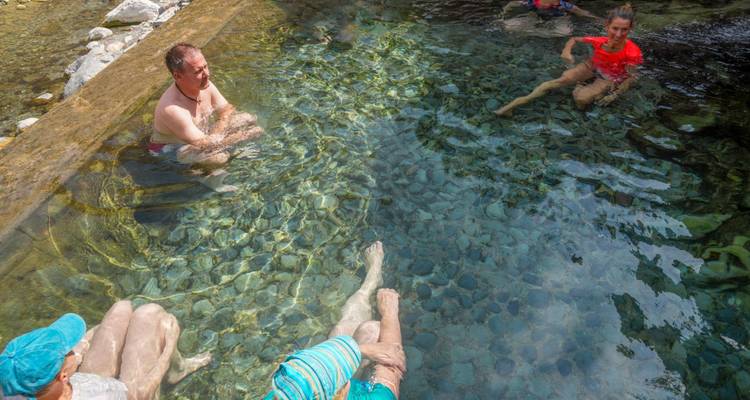 Les visiteurs se détendent dans un bassin naturel peu profond avec une eau cristalline et un environnement rocheux.