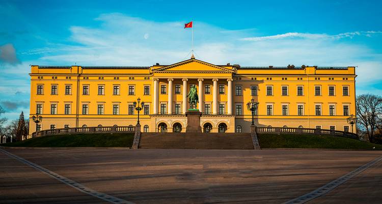 The stately yellow façade of Oslo’s Royal Palace glowing in late-day light under a blue sky.