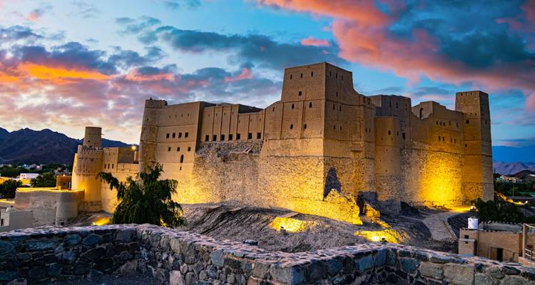 Le Fort de Bahla illuminé au crépuscule avec des nuages dramatiques et un arrière-plan montagneux à Oman.