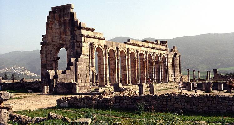 Les arches et colonnes romaines baignées de soleil des ruines antiques de Volubilis avec des montagnes brumeuses en arrière-plan