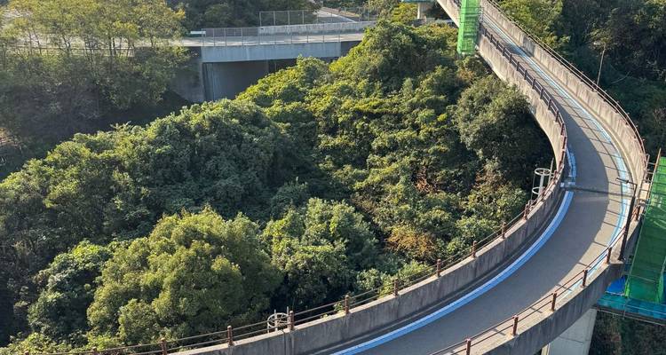 Eine erhöhte spiralförmige Rampenbahn schlängelt sich durch dichtes grünes Hügellandschaftsvegetation.