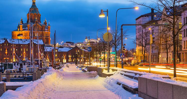 Snow-dusted waterfront promenade in Helsinki at twilight with Uspenski Cathedral illuminated in the background.