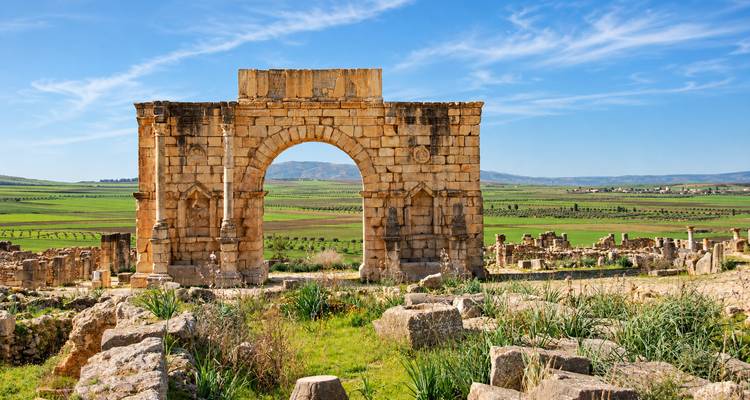 Arco triunfal de piedra de Caracalla que se alza en medio de llanuras verdes ondulantes y ruinas dispersas en Volúbilis.