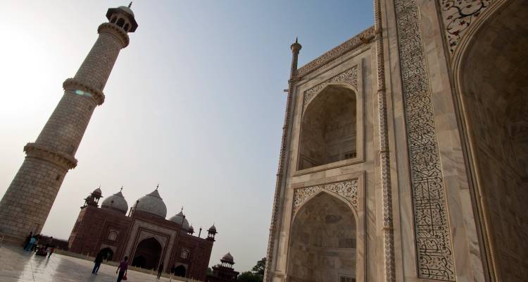 Vue latérale du complexe en marbre du Taj Mahal avec son minaret et sa mosquée sous un ciel dégagé.