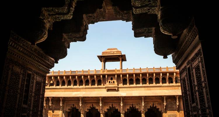Vue à travers une arche en grès sculpté dans la cour de Fatehpur Sikri avec une architecture moghole complexe.