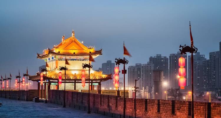 Illuminated ancient city wall tower at dusk with modern Xi’an skyline in the background and glowing red lanterns.
