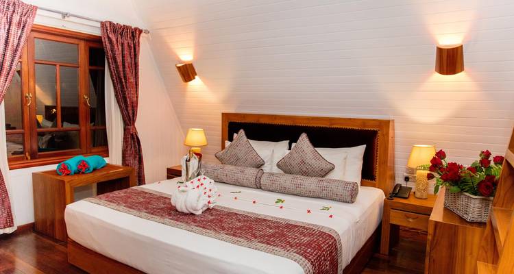 Chambre de resort accueillante aux murs blanc pur, mobilier en bois chaleureux et pétales de fleurs décoratives sur le lit.