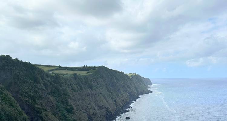 Steep green sea cliffs stretch along the Atlantic coast beneath a cloudy sky on São Miguel.