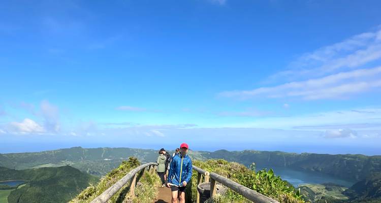 Hikers stand on a wooden viewpoint railing overlooking the volcanic caldera and lakes of Sete Cidades.