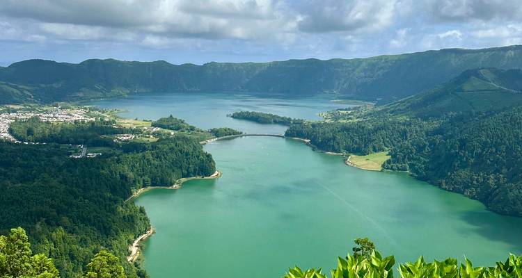 The twin green and blue lakes of Sete Cidades connected by a narrow bridge viewed from above.