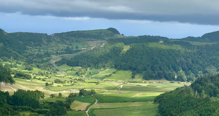 Verdant patchwork valley with winding rural roads under a band of low clouds.