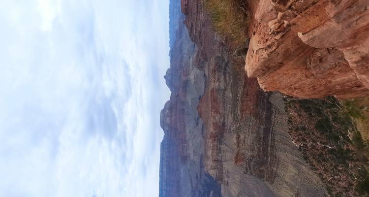Rugged red and gray layers of the Grand Canyon beneath a cloudy sky seen from the rim.