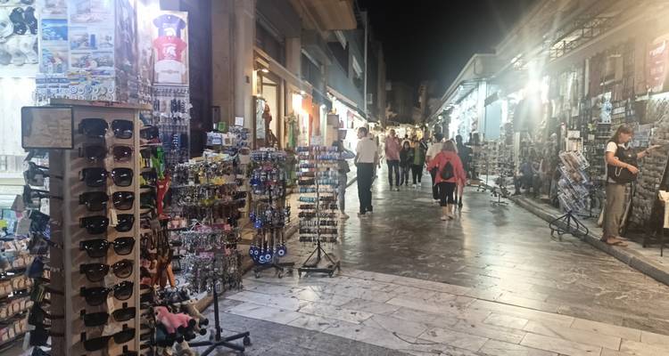 Ruelle animée de boutiques de souvenirs et de cadeaux à Athènes la nuit, bordée d'étals et de néons.