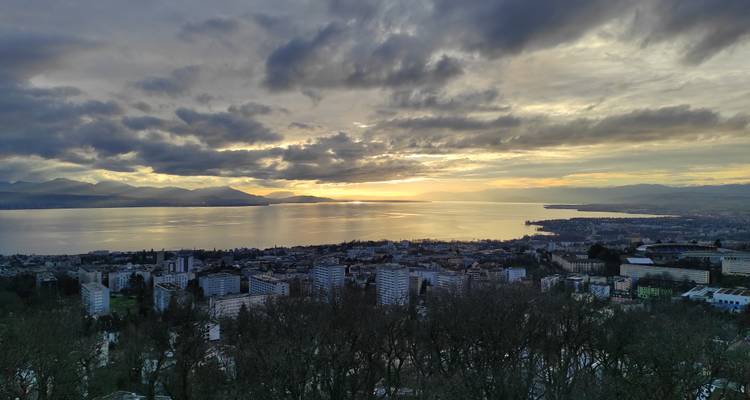 Vue panoramique sur le lac Léman au crépuscule avec des nuages dramatiques et un horizon doré.