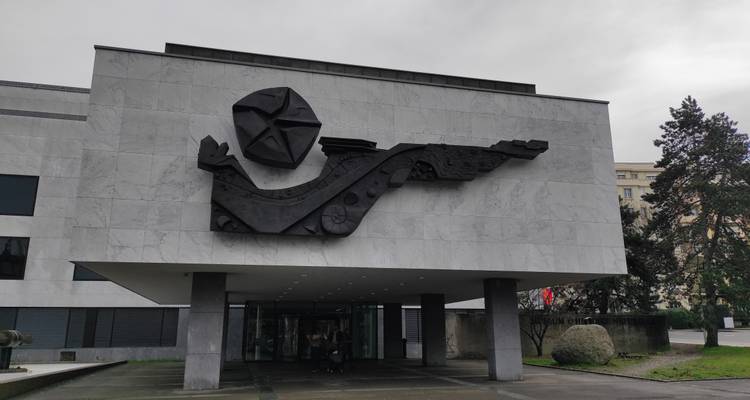 Bâtiment en marbre moderne avec une sculpture en bas-relief noir sur sa façade sous un ciel gris.