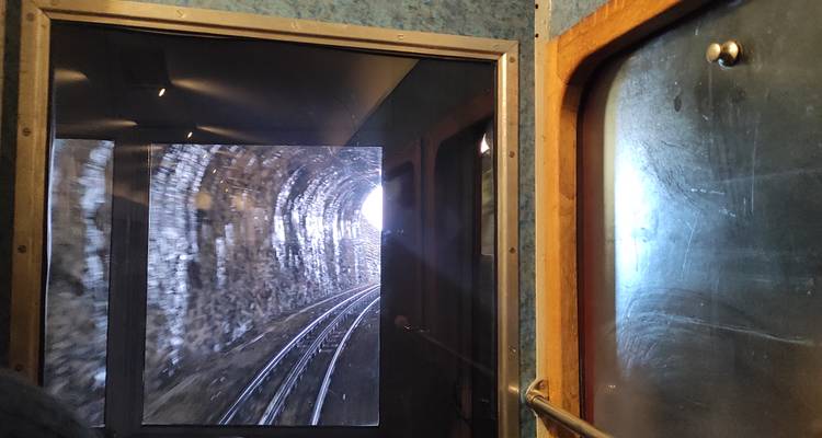 Vue de l'intérieur d'un tunnel de chemin de fer à crémaillère en montagne avec des voies ferrées qui se courbent vers la lumière du jour brillante