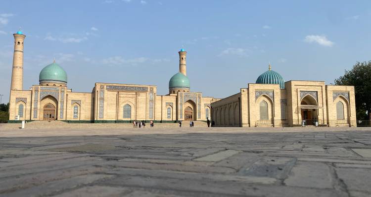Weitläufiger Platz mit mehreren Moscheen aus Ziegeln und türkisfarbenen Kuppeln, die sich gegen einen hellblauen Himmel abheben.