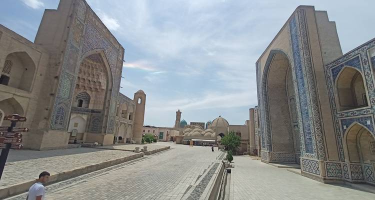 Steinweg, gesäumt von imposanten Eingängen gekachelter Madrasas und entferntem Minarett unter vereinzelten Wolken.