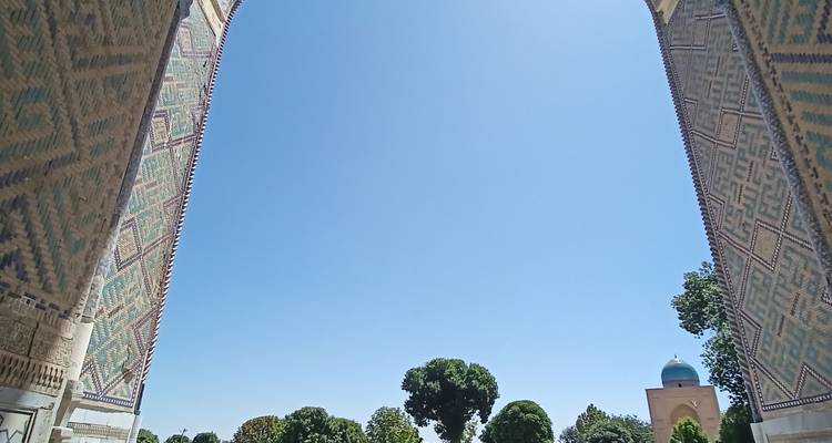 Blauer Himmel, gerahmt durch gemusterte Kachelbogen mit sichtbaren Gartenbaumen in der Ferne darunter.
